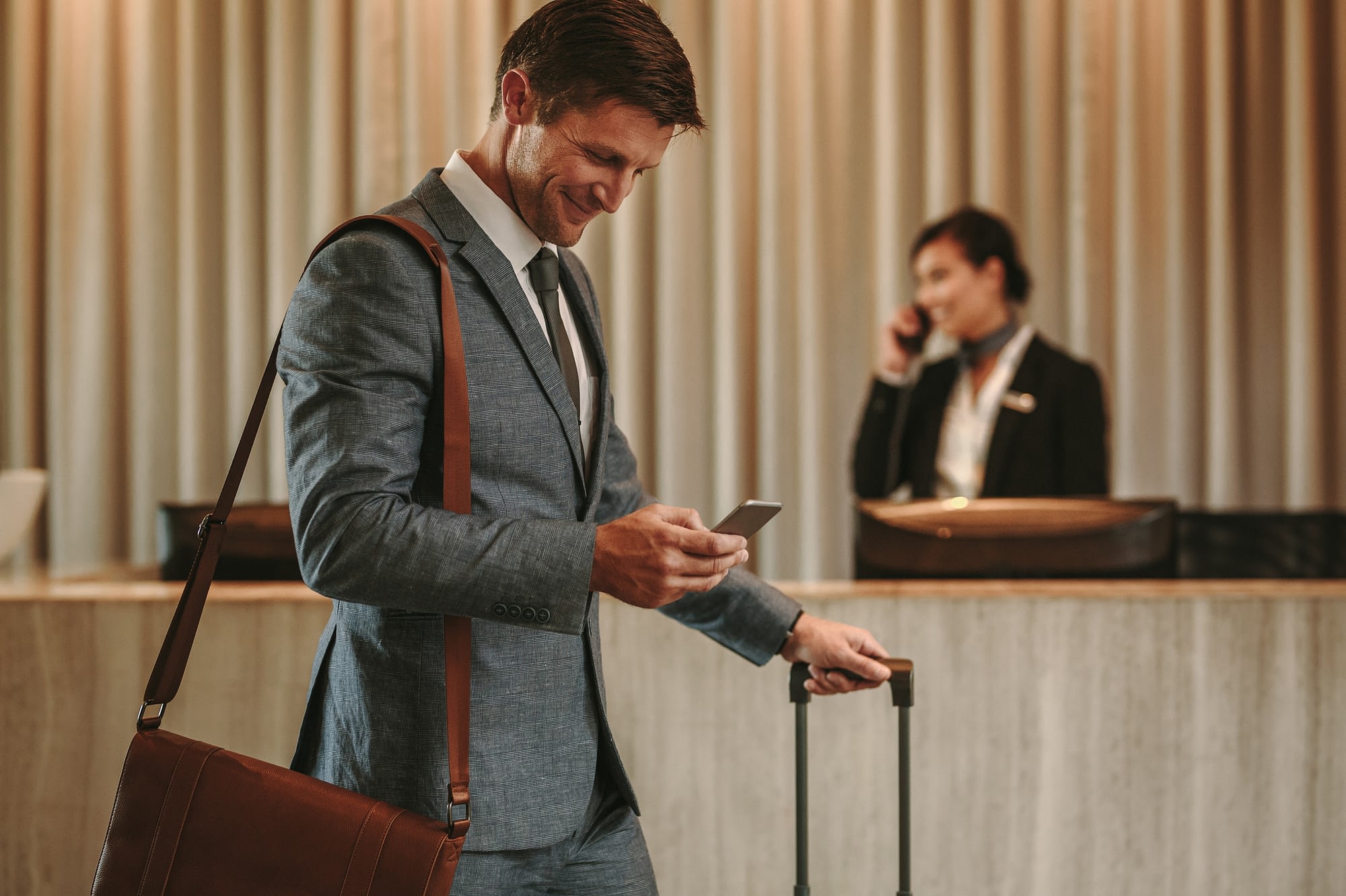 Happy hotel guest looking at phone in hotel lobby